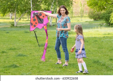 Young woman with a little six-year old girl flying a kite in a green park