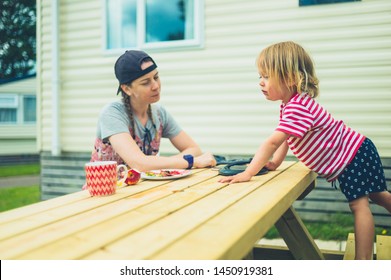 A Young Woman And A Little Toddler Are Sitting At A Table Outside In A Trailer Park