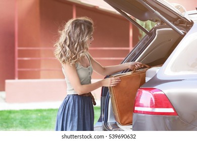 Young Woman Loading Suitcase Into Car Trunk