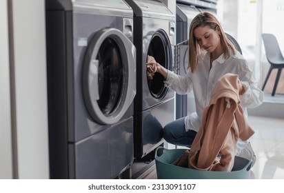 Young woman loading washing machine in public laundry. - Powered by Shutterstock