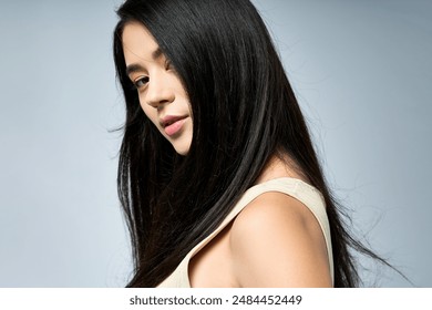 A young woman with long black hair strikes a stylish pose against a light blue background. - Powered by Shutterstock