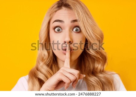A young woman with long blonde hair stands in front of a bright yellow background. She is looking directly at the camera with a surprised expression. She is holding her index finger to her lips