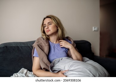 young woman with long covid syndrome - painful condition, headache, sitting on the couch at home - Shutterstock ID 2069308106