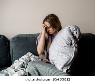 young woman with long covid syndrome - painful condition, headache, sitting on the couch at home - Shutterstock ID 2069308112
