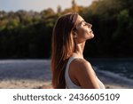 Young woman with long hair enjoying sun with closed eyes getting natural vitamin D outdoors. Peace of mind. Mindfulness, mental health,  spirituality, well-being, unwind yourself 