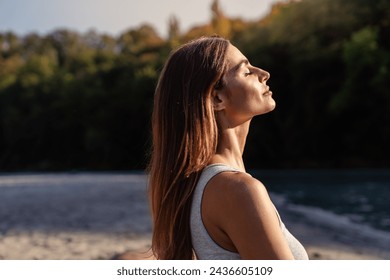 Young woman with long hair enjoying sun with closed eyes getting natural vitamin D outdoors. Peace of mind. Mindfulness, mental health,  spirituality, well-being, unwind yourself 