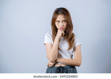 Young woman with long hair expressing contemplation and frustration with folded arms and hand on chin, white background. - Powered by Shutterstock