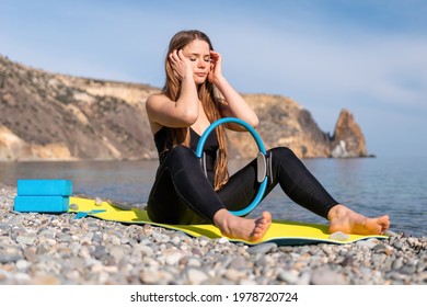 Young woman with long hair, fitness instructor in black Sportswear Leggings and Tops, stretching on a yoga mat with magic pilates ring near the sea on a sunny day, female fitness yoga routine concept - Powered by Shutterstock