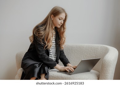 A young woman with long hair focuses on her laptop while seated on a stylish white couch in a modern office setting, working diligently on a project during daylight hours.