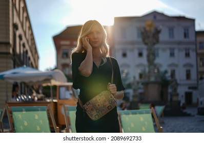 Young Woman With Long Hair Talking On Her Cell Phone, Blurred City With Strong Backlight Behind Her