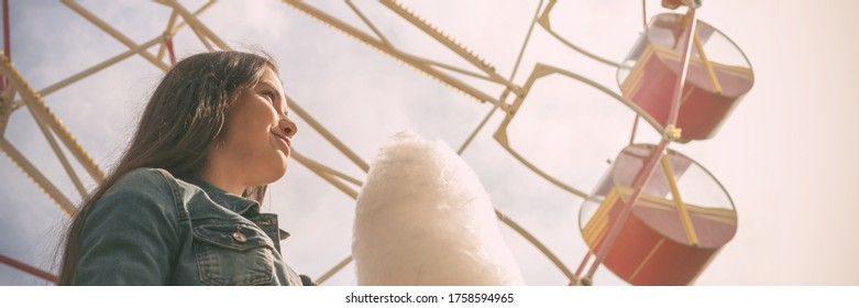 young woman with long loose flowing hair holds cotton candy standing against coloured ferris wheel low angle shot - Powered by Shutterstock