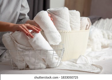 Young Woman With Long Red Hair Is Sitting On Bed And Folding Clean White Hand Towels Into Mesh Basket In Bedroom. Stack Of Roll Up Towels With Copy Space. Neat And Tidy Linen. Hypoallergenic Textile.