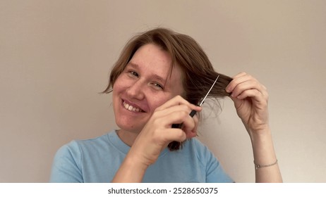 young woman with long red or light brown hair holding scissors in hands and smiling at camera, concept haircut, split ends - Powered by Shutterstock