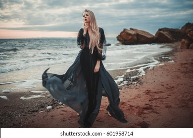 Young woman in long transparent black dress among beach and sea. Wind blows hem of her dress. - Powered by Shutterstock