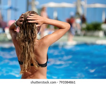 Young Woman With Long Wet Hair Is Sitting Against The Swimming Pool.