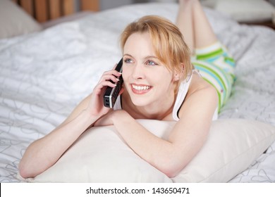 Young Woman Looking Away While Conversing On Cordless Phone While Lying In  Bed