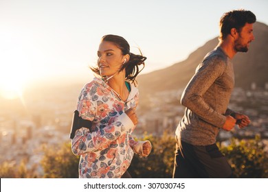 Young Woman Looking Back While Running With A Man Outdoors. Couple On Morning Run.