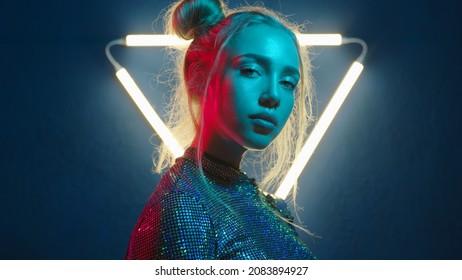 Young woman looking at the camera in the neon light of the club. Camera zoom. Portrait of a beautiful futuristic girl close-up. Lady in multicolor glow.
