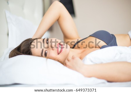 Young woman looking at camera and smiling while lying on the bed