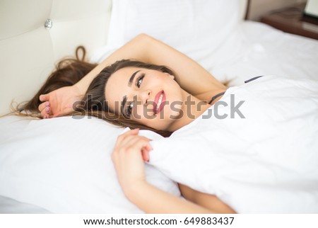 Young woman looking at camera and smiling while lying on the bed
