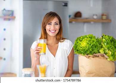 Young woman looking at camera while drinking orange juice in the kitchen at home. Woman with healthy food indoors. Morning routine. Young woman enjoying fresh orange juice - Powered by Shutterstock