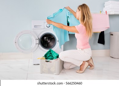 Young Woman Looking At Clothes After Washing In Washing Machine At Utility Room
