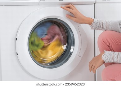 Young Woman Looking At Clothes Rotating Inside The Washing Machine In Kitchen At Home - Powered by Shutterstock