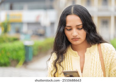 Young woman looking concerned while reading a message on her smartphone in a park - Powered by Shutterstock