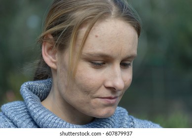 A Young Woman Looking Down With A Slight Smirk On Her Face On A Sunny Day