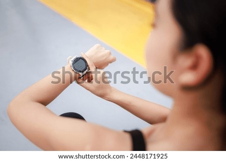 young woman looking down at the timer on her wrist to time before jogging in the morning.