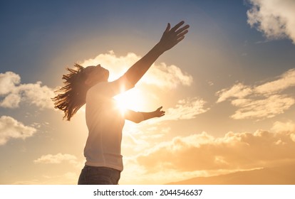 Young woman looking up feeling energized by the warm rays of sunshine lifting arms up to the sunset sky. Letting go of your fears concept.  - Shutterstock ID 2044546637