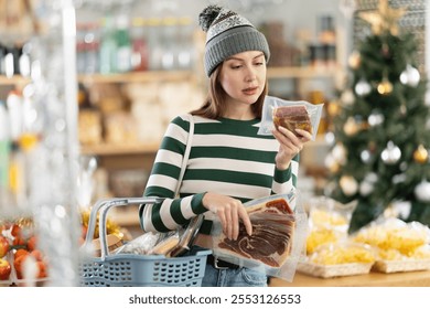 Young woman is looking at hamon in store. Market visitor chooses suitable piece of meat delicacy. She took several different varieties of vacuumed hamon , reads labels and examines product - Powered by Shutterstock