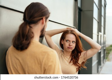 Young woman looking at her boyfriend in disbelief puffing out her cheeks with a sideways glance as they chat on an urban street