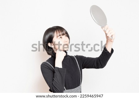 Young woman looking at her face in a hand mirror