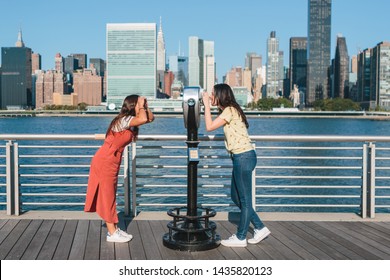 Young woman looking at her friend through a tourist binocular during her summer vacation in New York