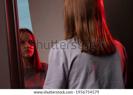 Young woman looking at her mirror reflection with grief. Unhappy sad person. Psychological concept of mental disorders and self esteem.