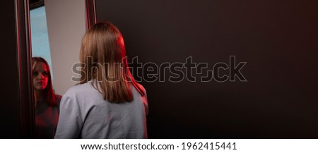 Young woman looking at her mirror reflection with grief. Unhappy sad person. Psychological concept of mental disorders and self esteem. Banner with copy space.