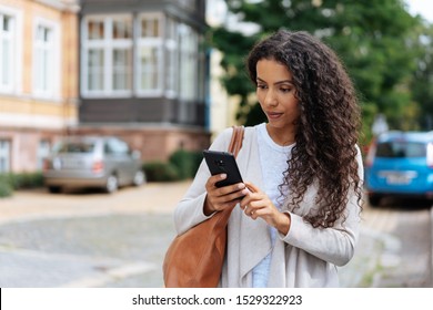 Young woman looking at her mobile phone in consternation as she reads a text message outdoors in a town street - Shutterstock ID 1529322923