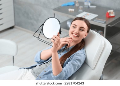 Young woman looking at her new dental implants in mirror indoors - Powered by Shutterstock