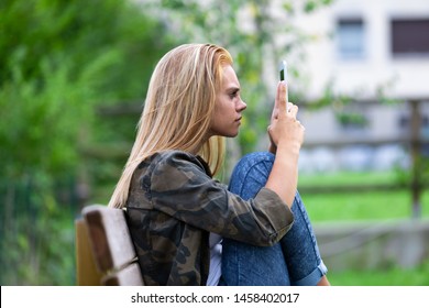 young woman looking at her tablet on consternation lifting it close to her eyes as she relaxes in the garden on a bench