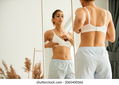 Young woman looking herself in a mirror while doing breast self-exam at home. 