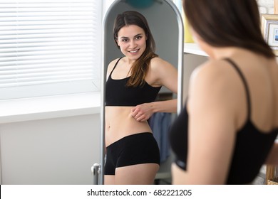 Young Woman Looking At Herself In The Mirror And Pinching Her Stomach Fat