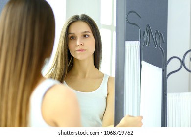 Young woman looking herself reflection in mirror at home