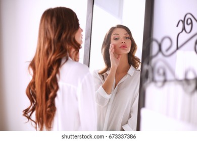 Young woman looking herself reflection in mirror at home