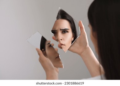 Young woman looking at herself in shard of broken mirror on light grey background, closeup - Powered by Shutterstock