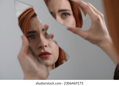 Young woman looking at herself in shard of broken mirror on light grey background, closeup - Powered by Shutterstock