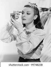 Young Woman Looking Into A Mirror And Putting On Make Up