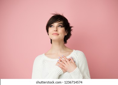 Young Woman Looking Up To The Left Corner With Hands On Chest. Happy Smiling Woman Feels Grateful, Hopes For Successful Plan Realization, Believes In Success, Wishes Dream Come True, Visualizes Future