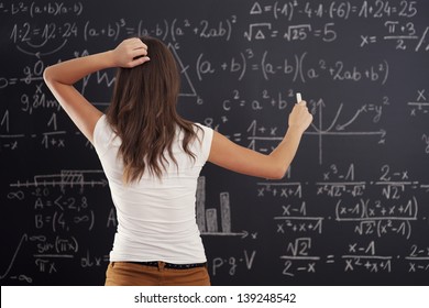 Young Woman Looking At Math Problem On Blackboard