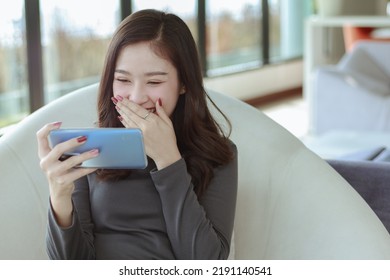 young woman looking movies series at smartphone sitting on sofa in living room 